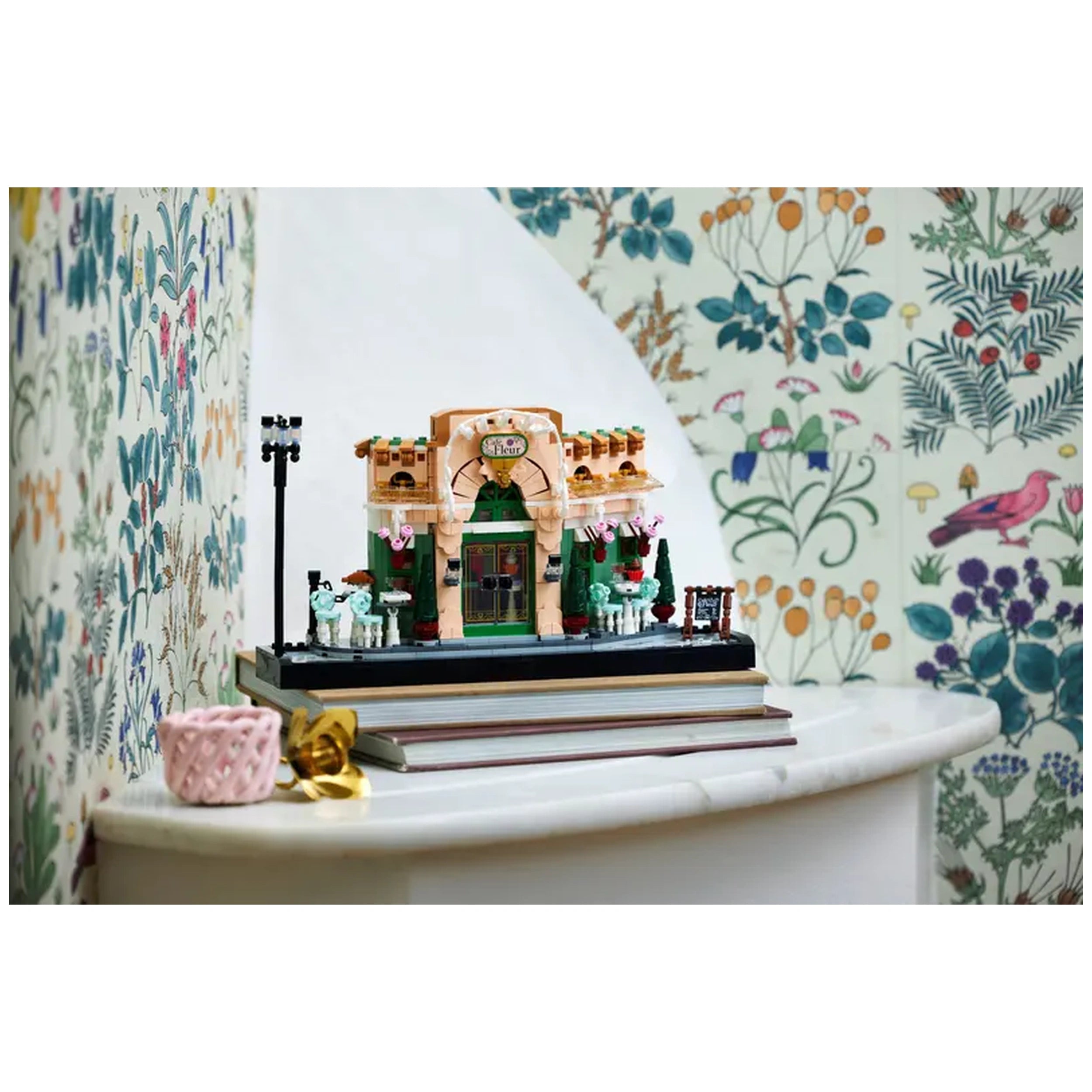 LEGO® Icons French Café construction set displayed on stacked books, featuring detailed café architecture and potted plants.