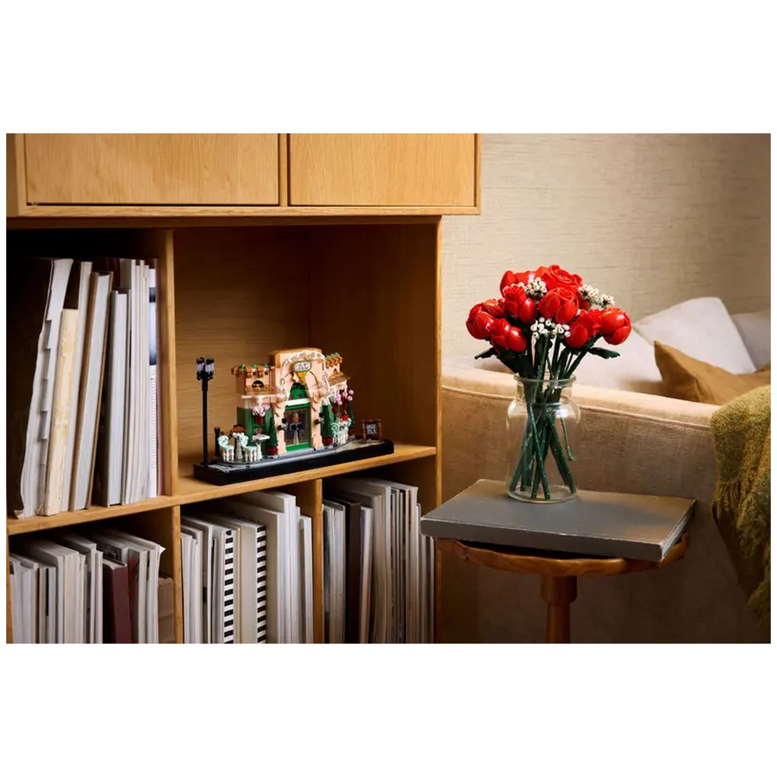 LEGO® Icons French Café set displayed on a wooden shelf, surrounded by books, with a vase of vibrant red roses on a nearby table.