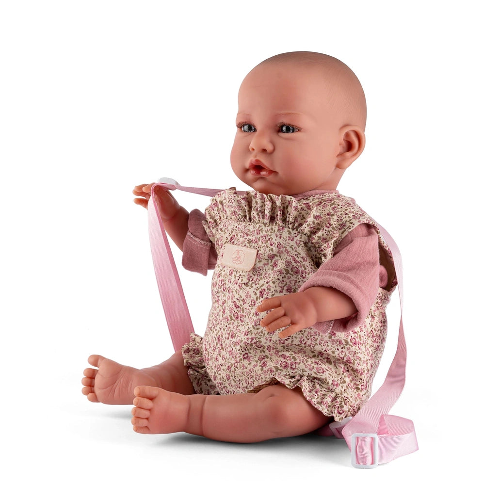 Realistic baby doll in a floral romper with pink sleeves and straps, sitting upright.