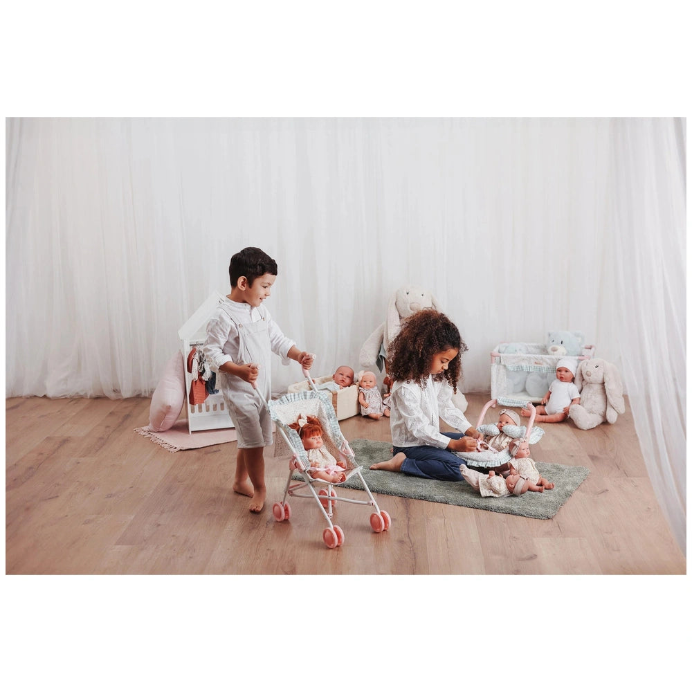 Young children playing with Asi Dolls and a Cloe Small 56 cm stroller in a cozy room with stuffed toys and doll accessories.