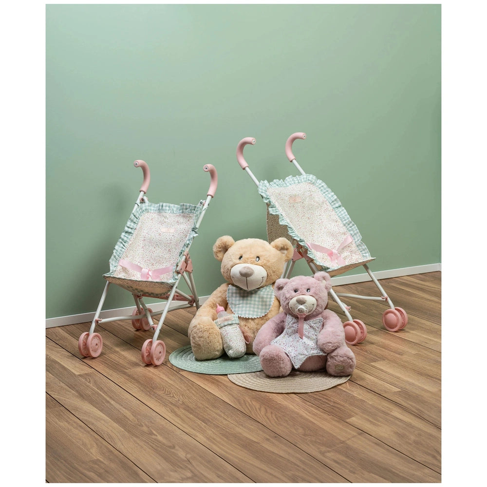 Toy strollers with pink handles beside two plush teddy bears on wooden floor, against a soft green wall.