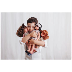 Child smiling while holding three ASI Dolls from the Jara Collection, featuring elegant outfits and diverse hairstyles.