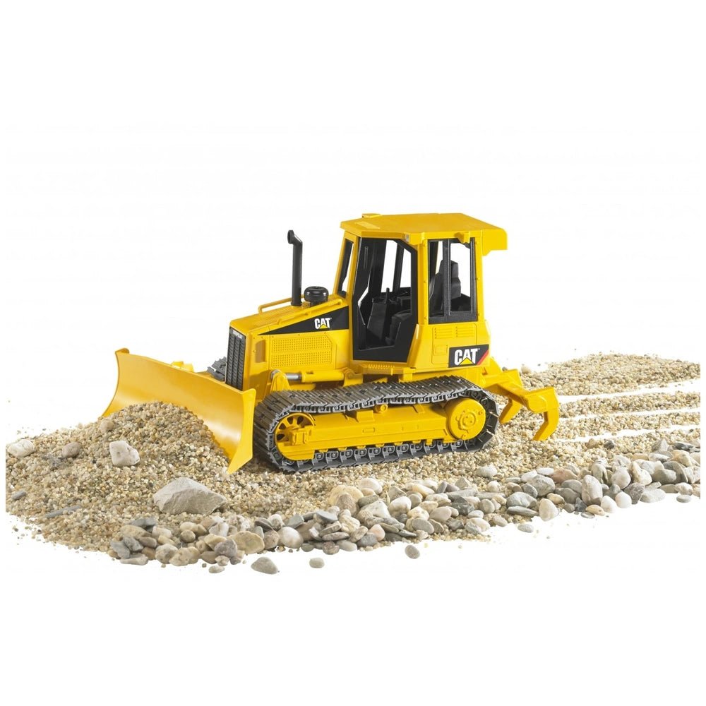 Yellow Bruder CAT track-type tractor toy on gravel, showing adjustable blade and ripper for realistic construction play.