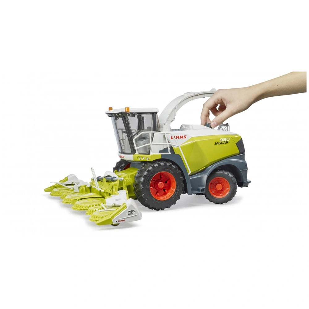 Hand operating Bruder Claas Jaguar 980 Field Chopper toy with green and white corn header, large wheels, and detailed design.