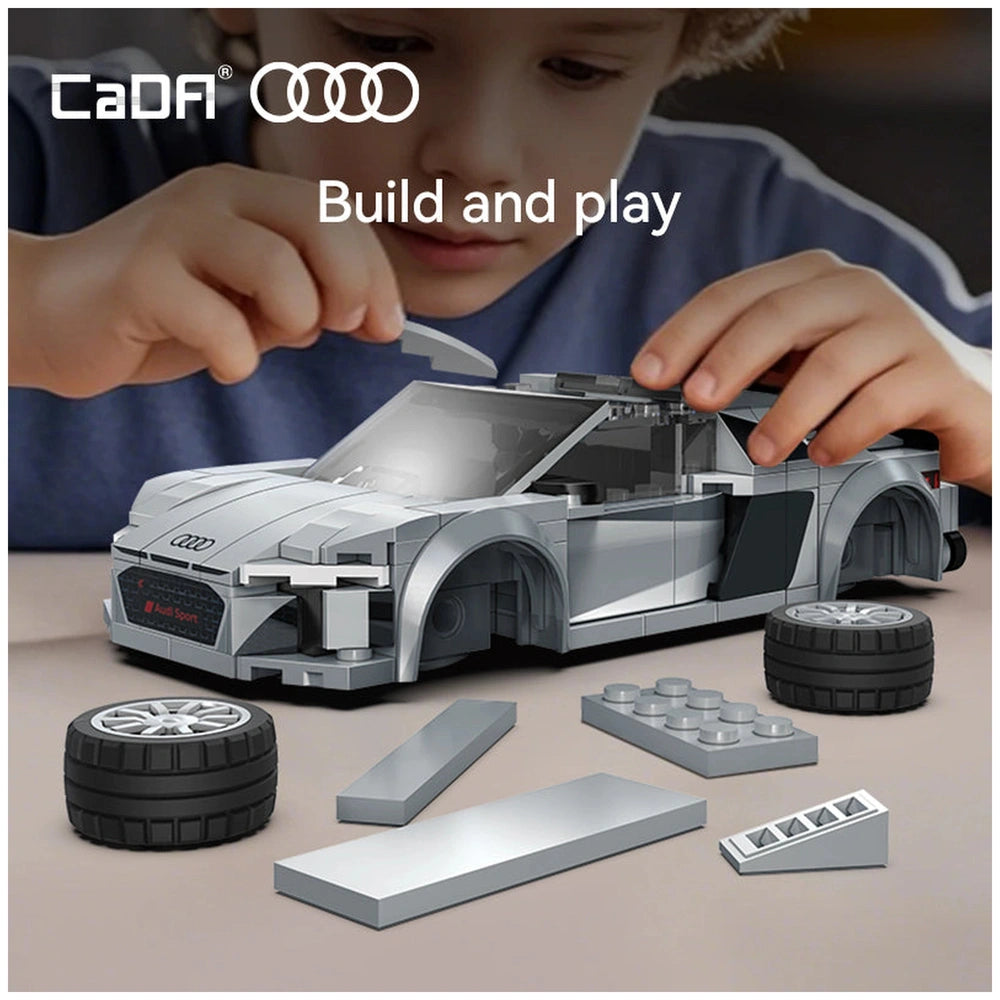 Cada Bricks 1:24 Audi R8 Coupe in silver, built with gray LEGO bricks, rubber tires, and a child's hands assembling it.