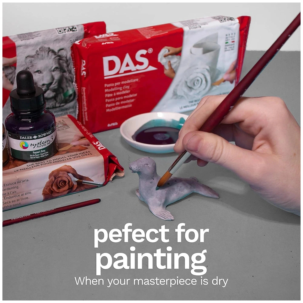 Das Modeling Clay in terra-cotta packaging with various paintbrushes on a gray surface.