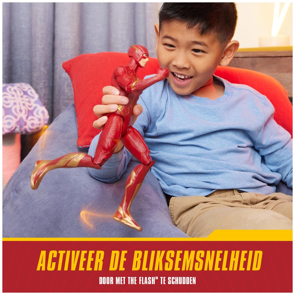 The Flash action figure in a dynamic pose is held by a smiling boy on a red couch, showcasing vibrant colors and excitement.