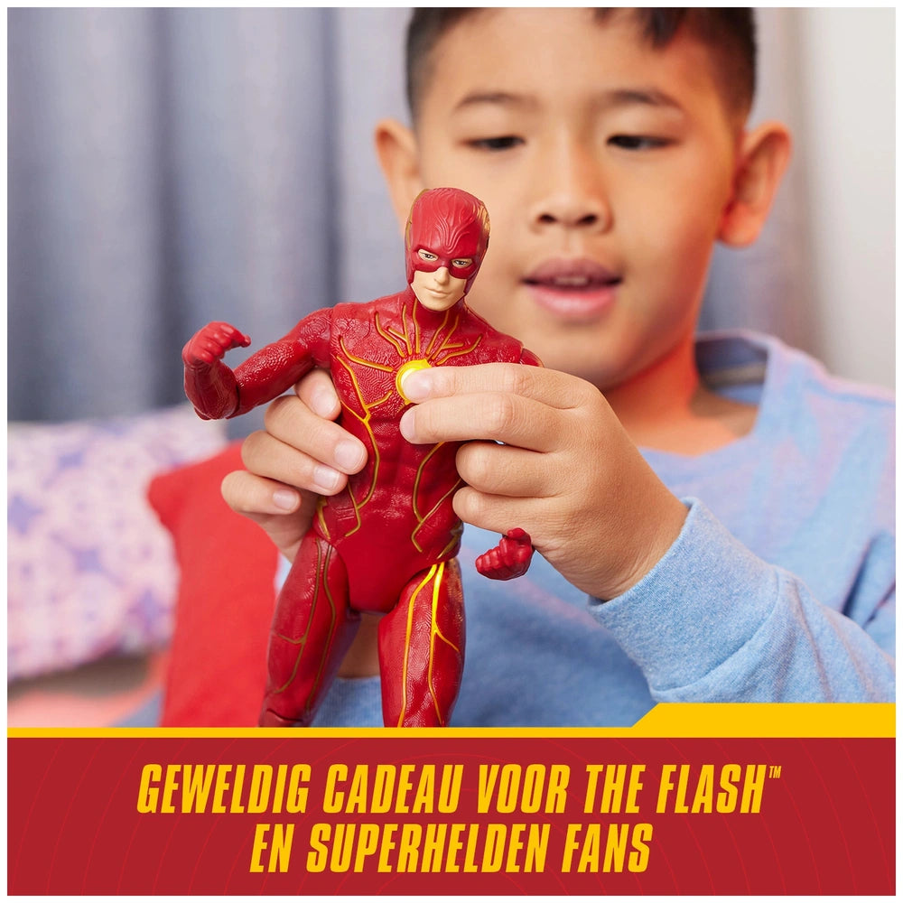 The Flash action figure in red and yellow is held by a child indoors, excitedly showcasing its lights and sounds.