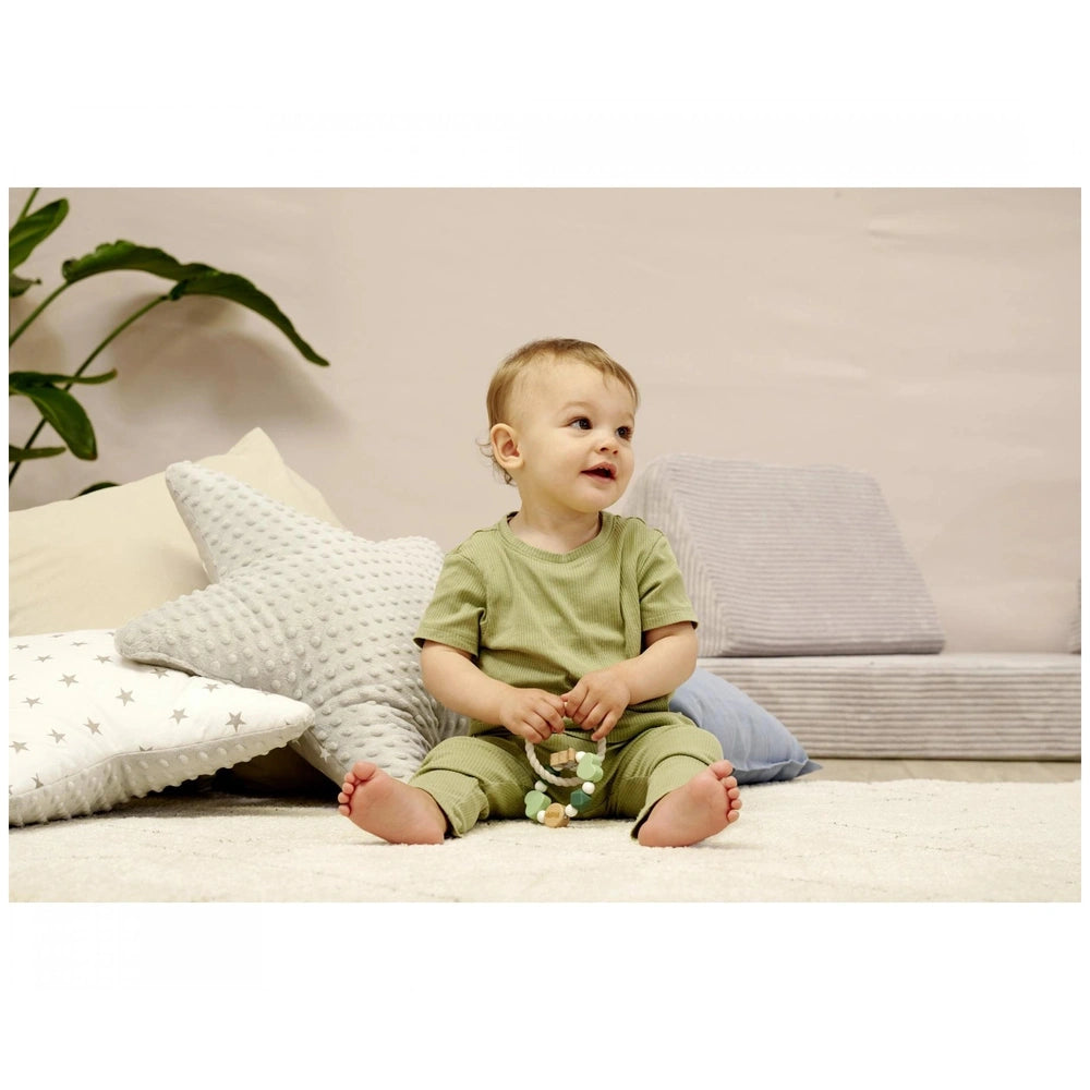 Eichhorn Baby HiPP Grapper with Ring is featured as a young child in a green outfit sits on a white carpeted floor.