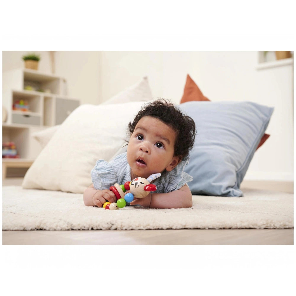 Eichhorn baby wooden teething ring rabbit rests beside a baby on a soft white rug in a cozy indoor nursery setting.