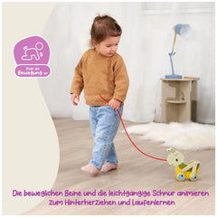 Colorful pulling grasshopper toy being tugged by a child in a brown sweater and blue jeans on a light wooden floor.
