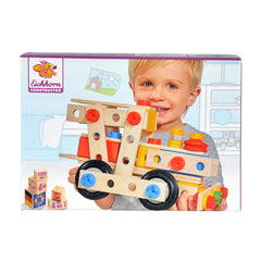 A young child with blonde hair smiles while holding a wooden construction toy against a colorful background featuring playful