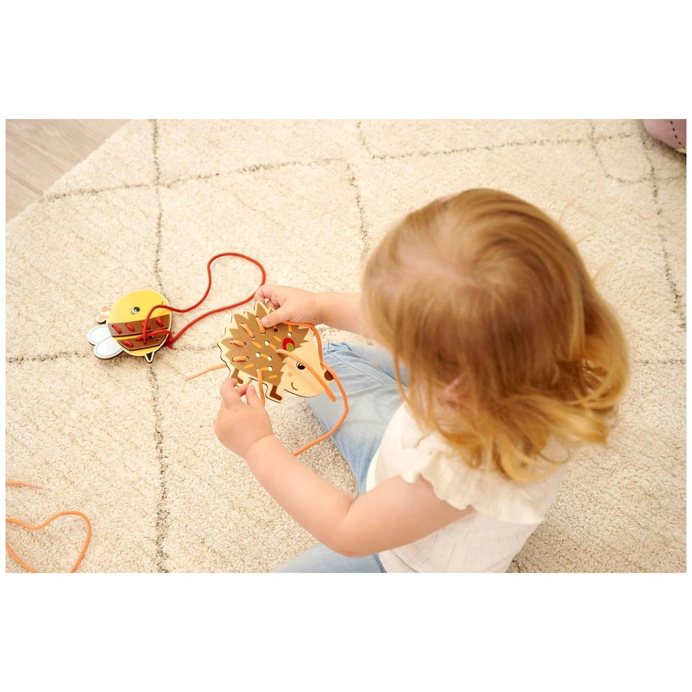 Eichhorn string game features a colorful sun toy with a red string, engaged with a young child on a beige carpet.