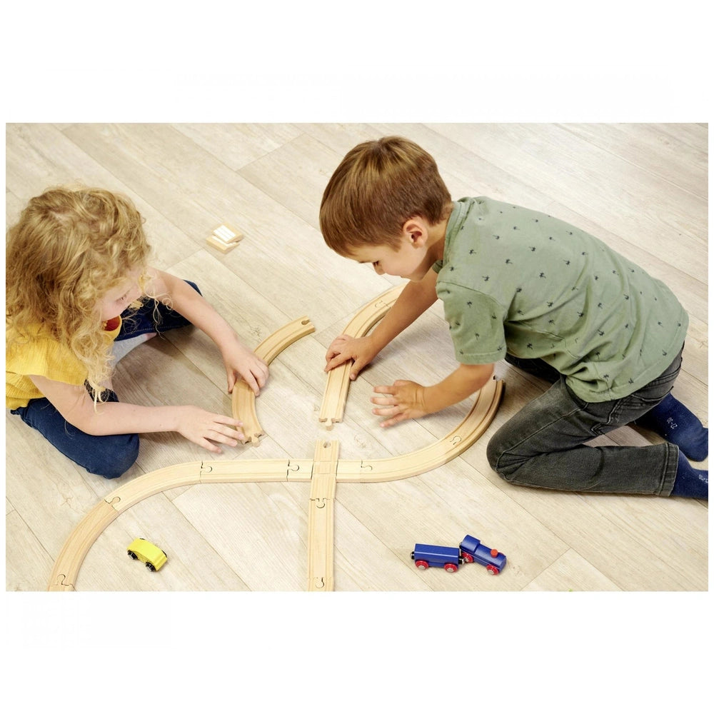 Eichhorn Train Track playset with children assembling wooden tracks and playing with toy trains on a wooden floor indoors.