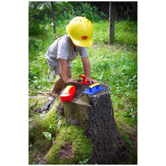 Gowi Design Bricklaying Set with a child in a yellow helmet, holding red and yellow and blue objects on a grassy stump.
