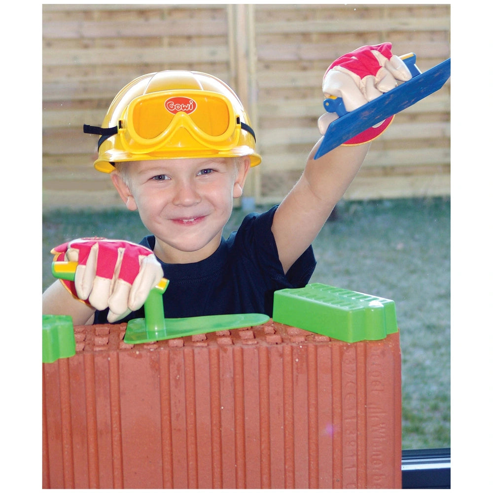 Gowi Design Bricklaying Set features a young boy in a yellow hard hat and red gloves holding a blue and white shovel by a bri