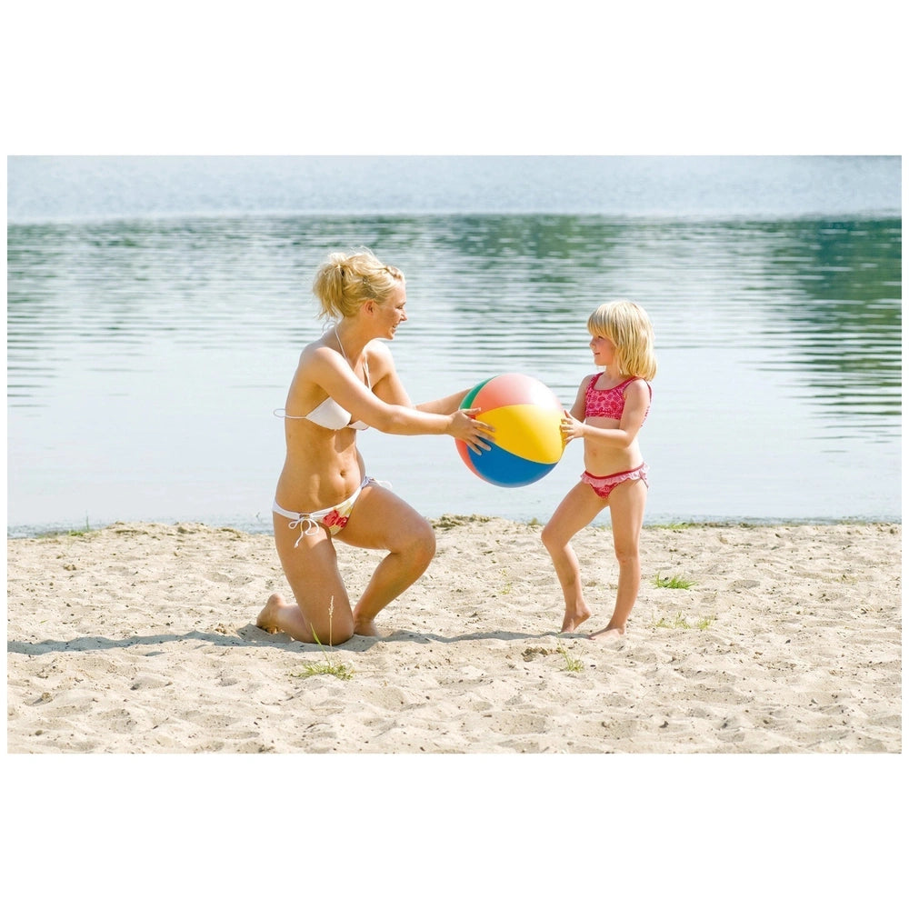 a colorful beach ball while playing with a young girl in a sandy beach setting.