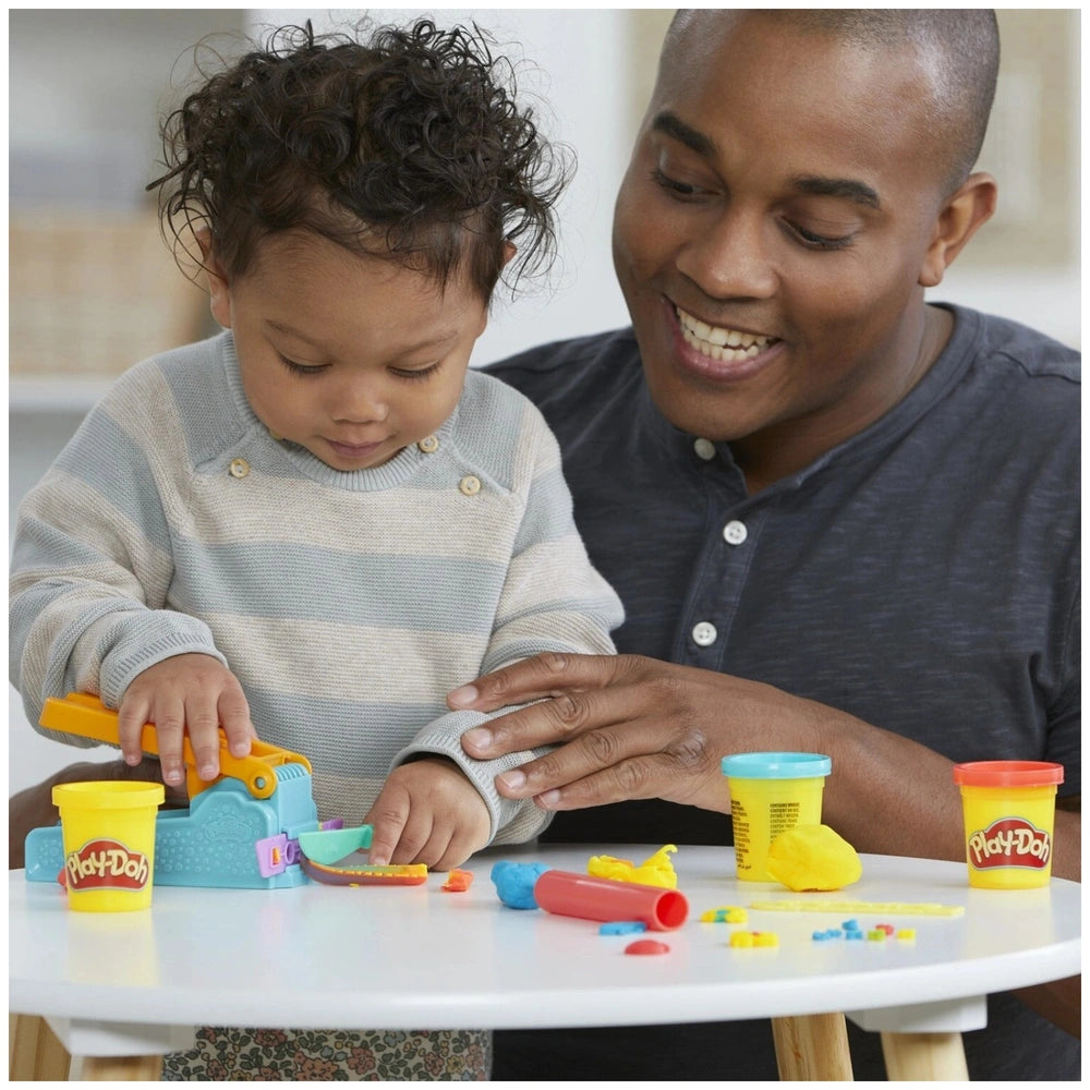 Hasbro Play-Doh Fun Factory Starter Set features a child in a gray and white striped shirt and a man in a blue shirt at a whi