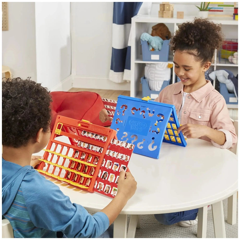 Hasbro Wer Ist Es Board Game displayed on a white table with two children holding red and blue plastic trays in a bright room