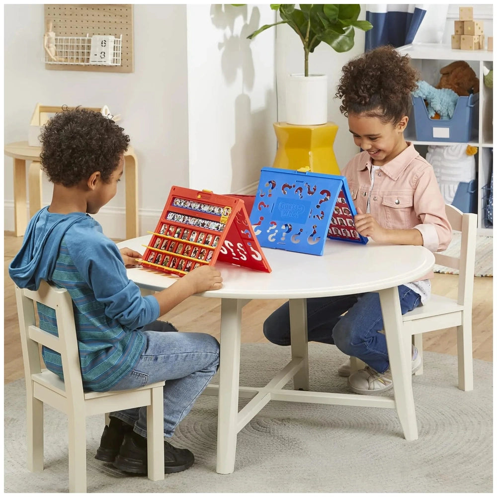 Hasbro Wer Ist Es Board Game on a white table with two children and red and blue toy laptops in a cozy setting.