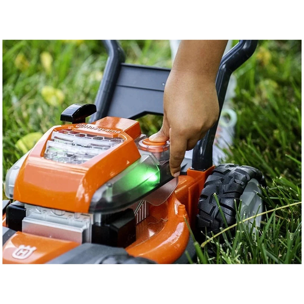 Husqvarna toy lawn mower with orange plastic body, black handle, and green wheels, set against a grassy background.