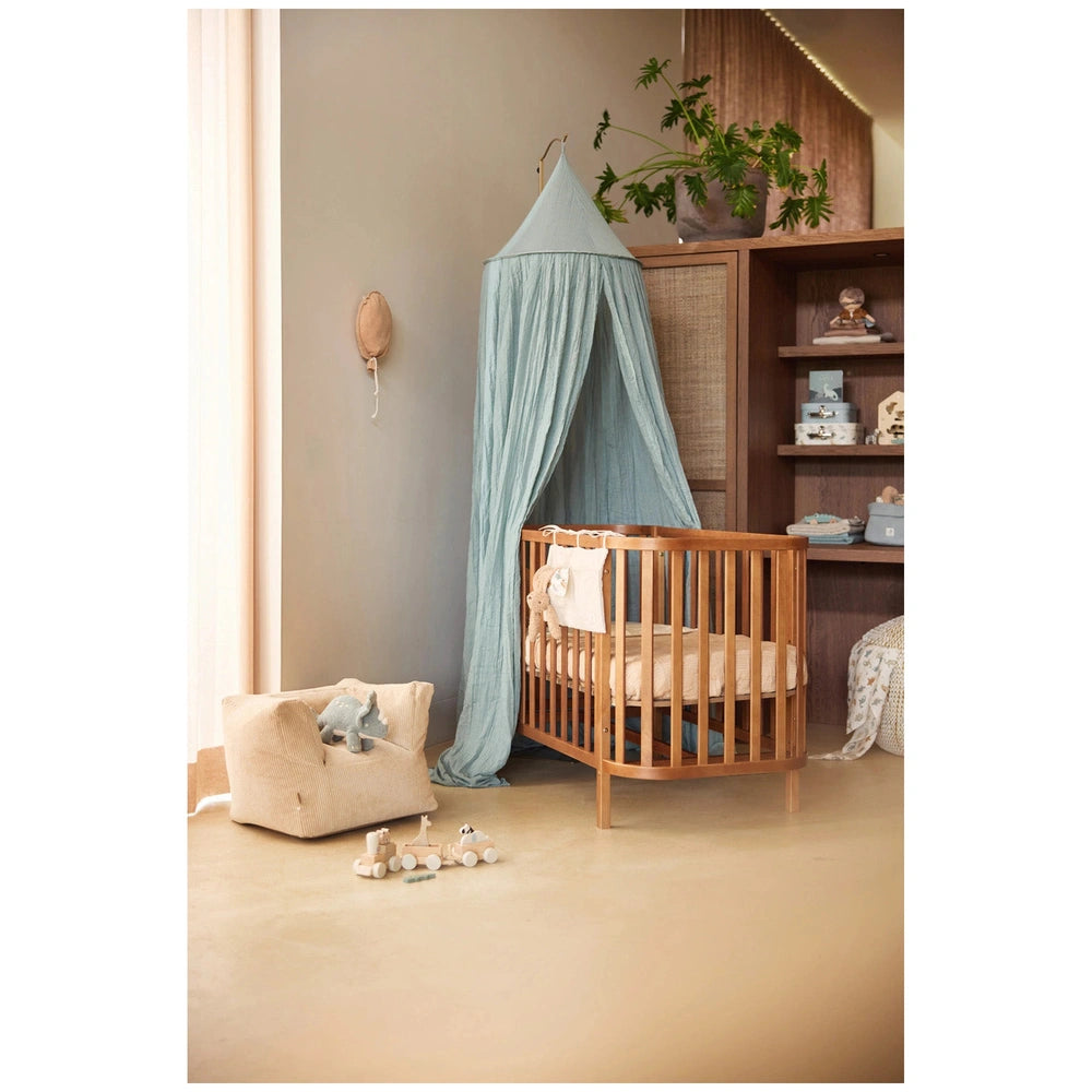 Jollein pacifier cloth bunny on a plush toy-strewn wooden crib with a fabric canopy, surrounded by a serene nursery setting.