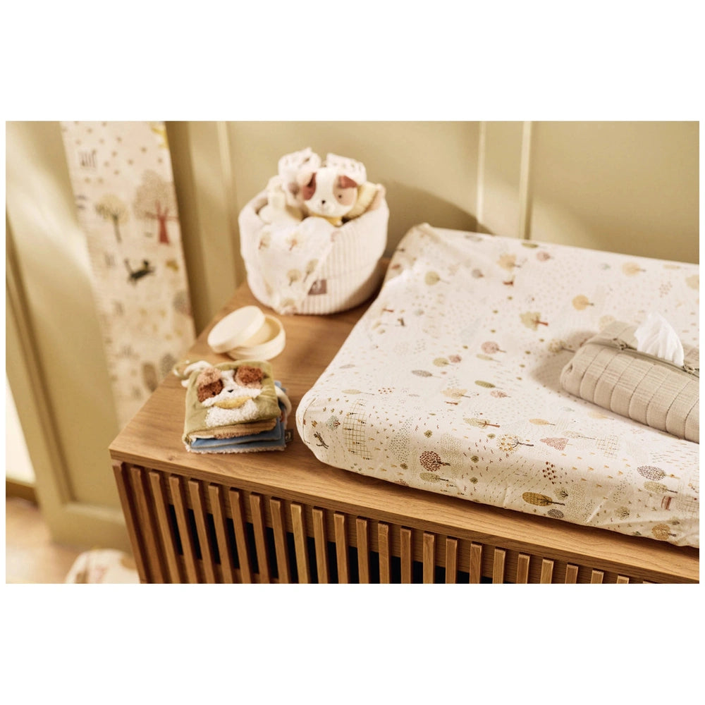 Jollein soft activity book displayed on a brown wooden surface, surrounded by floral patterned fabric and plastic items.