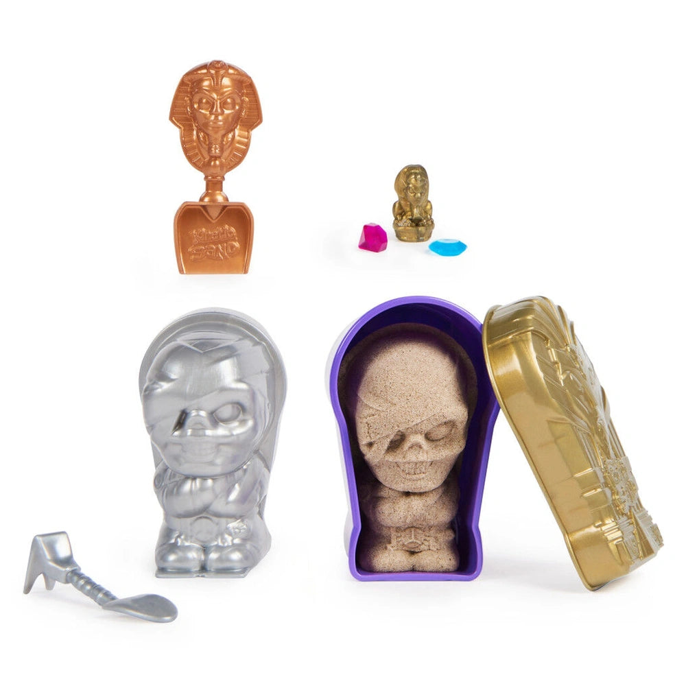 Kinetic Sand Mummy Tomb features a shiny silver shovel, sandbox, brown skull, and two small blue items on a white surface.