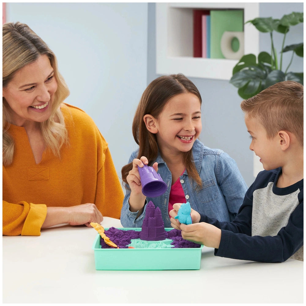 Kinetic Sand Sandbox Set displayed on a white table with a woman and two children happily engaged in play.