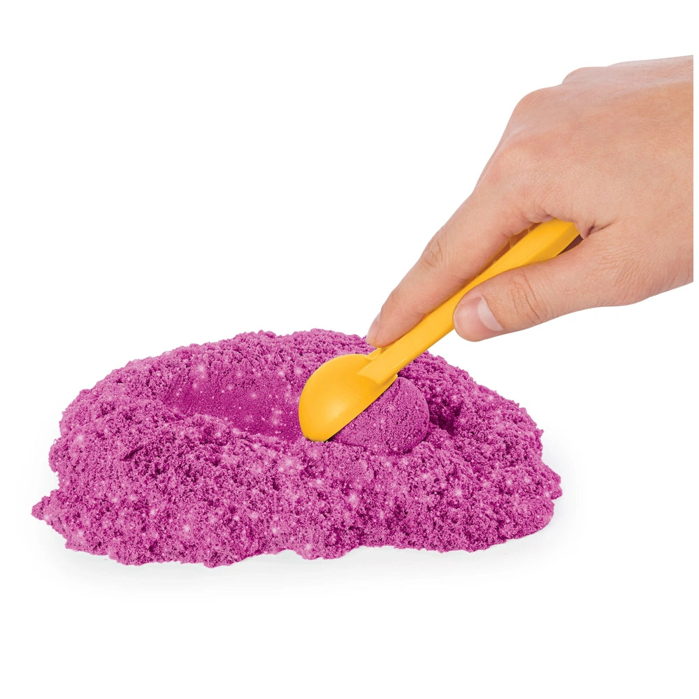 Kinetic Sand Shimmer Sparkle Sandcastle Set featuring a yellow plastic spoon resting on purple powdery sand.