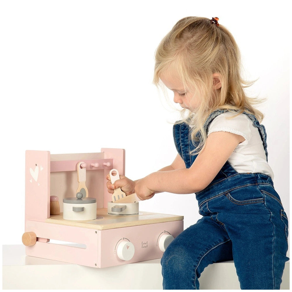 Foldable cooker toy in pink and white, held by a child in a denim jumpsuit, featuring multiple interactive white components.