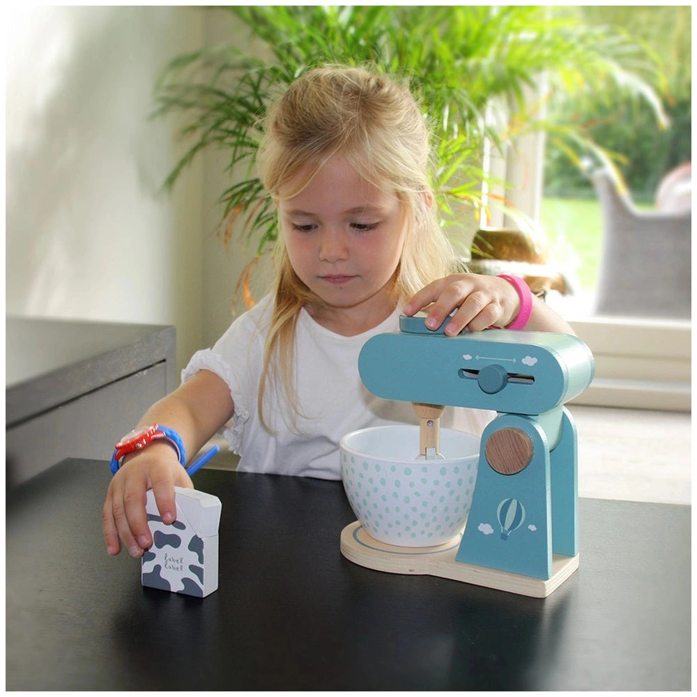 Blonde girl in a white shirt plays with a blue food processor on a black tabletop, with a green potted plant in the backgroun