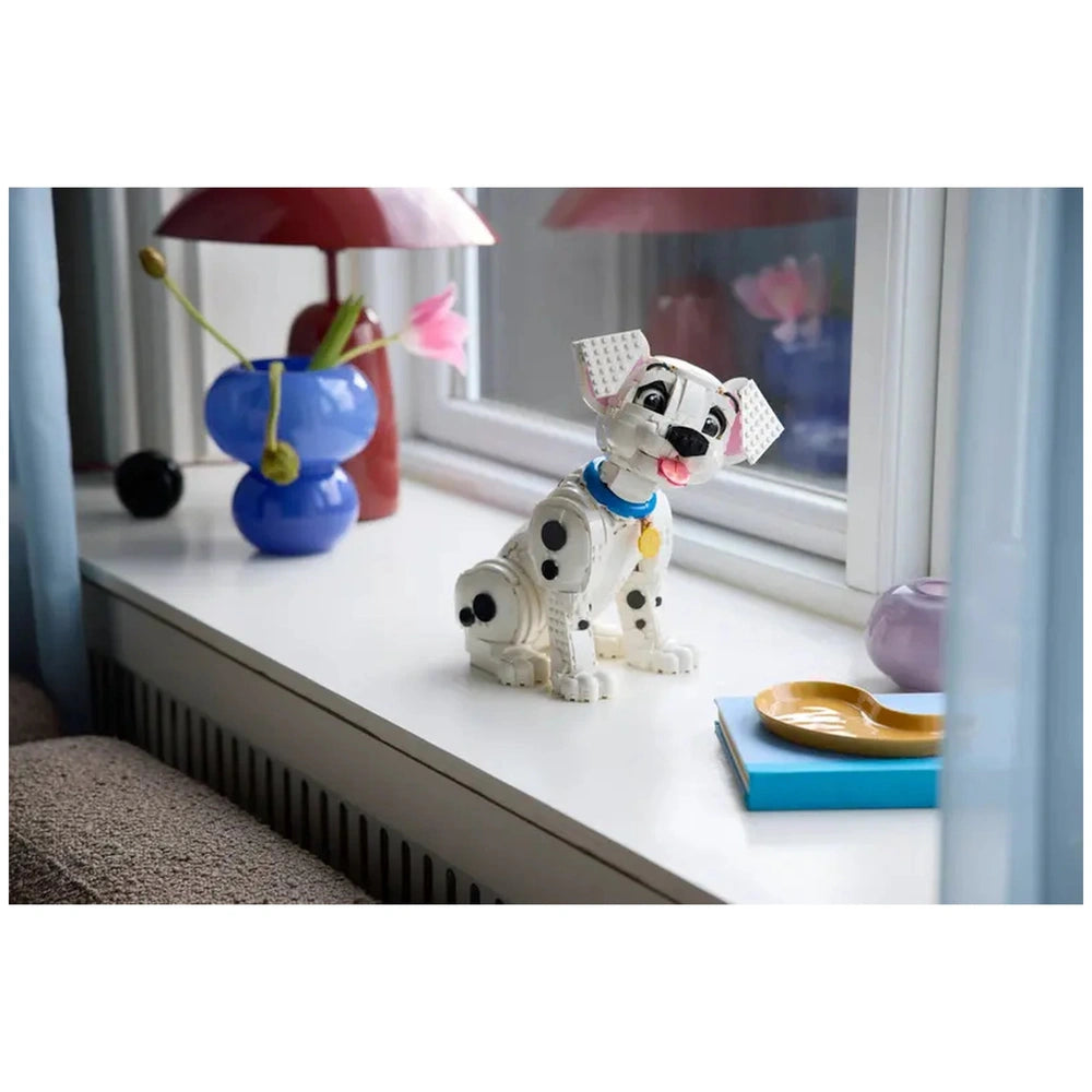 LEGO Dalmatian figurine sits on a window sill alongside a blue vase and bowl, creating a charming indoor scene.