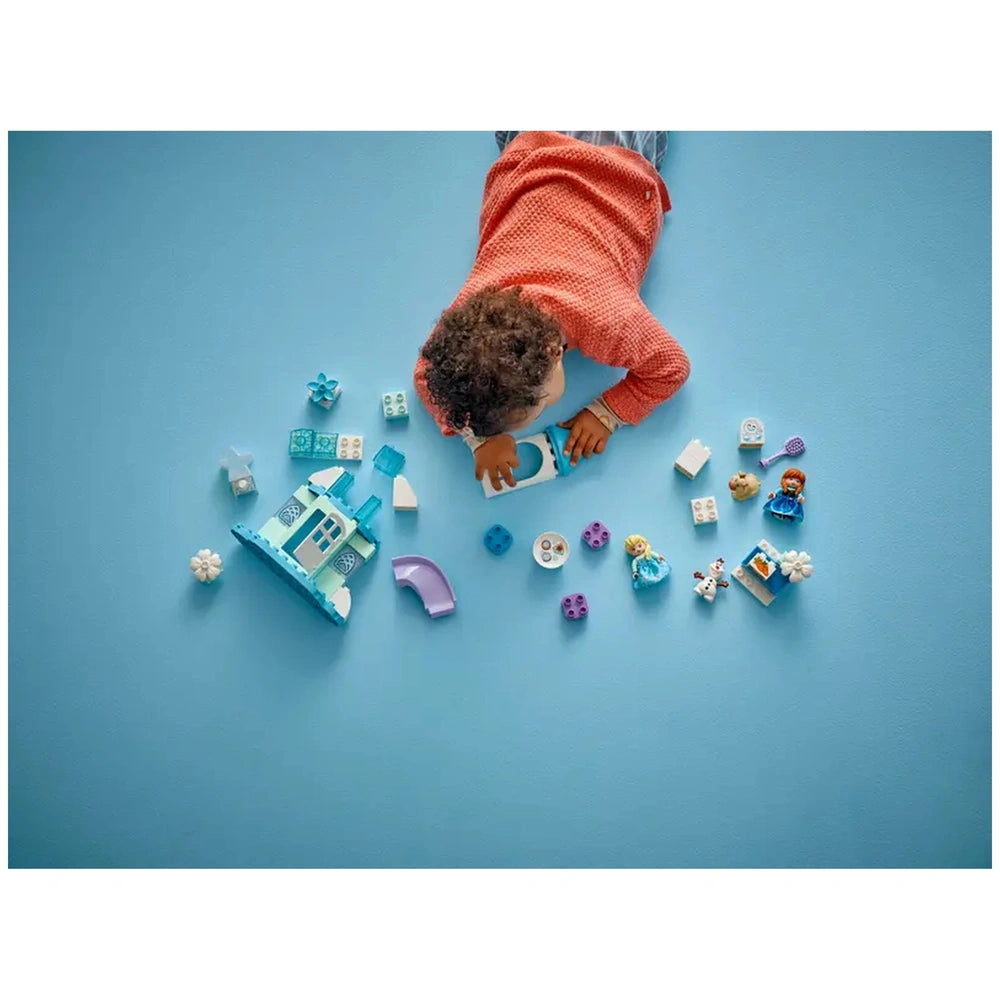 LEGO Anna and Elsa's Frozen Castle Party construction set is being played with by a child on a solid blue surface.