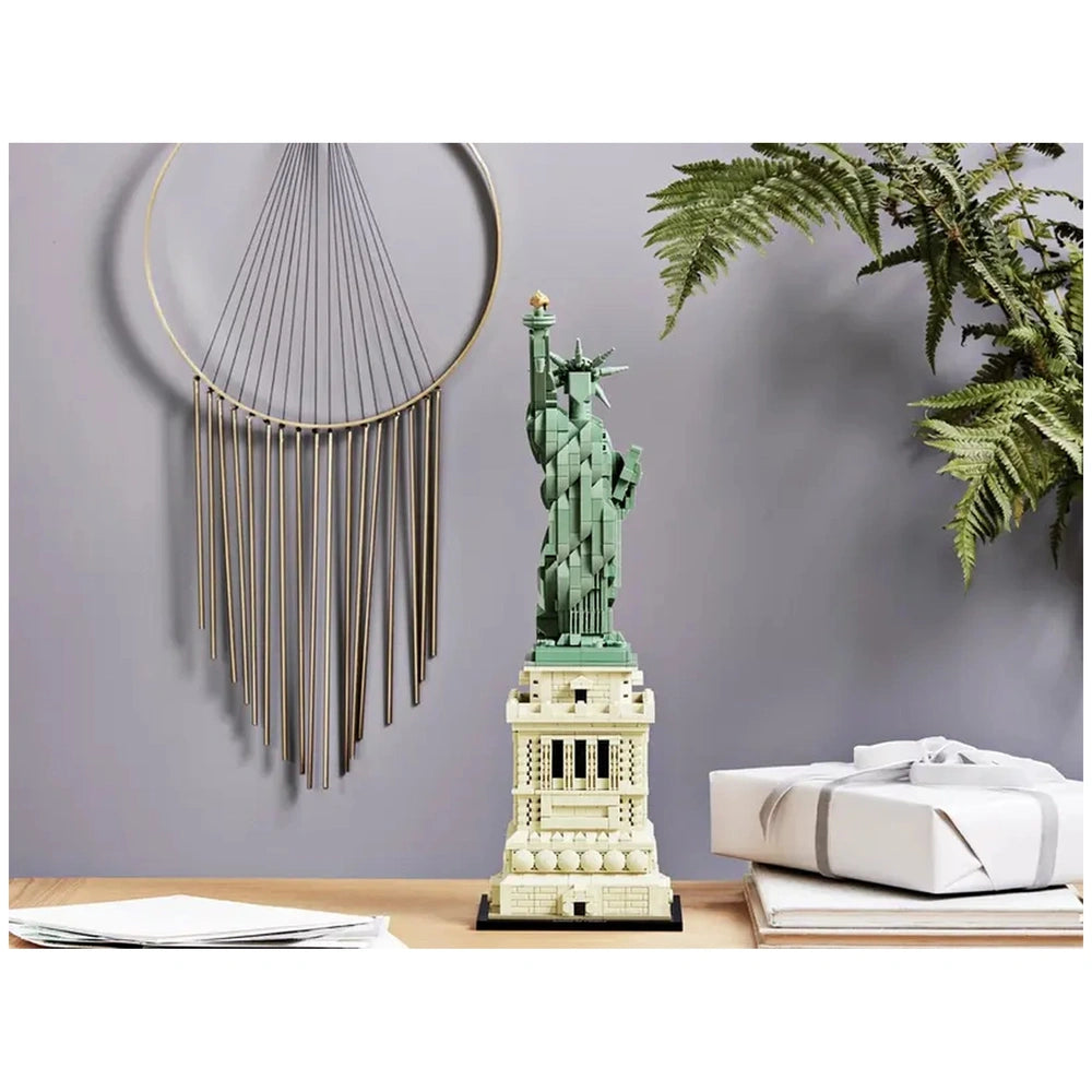 Lego Architecture Statue of Liberty miniature replica on a wooden pedestal, set against a textured wall and potted plant.