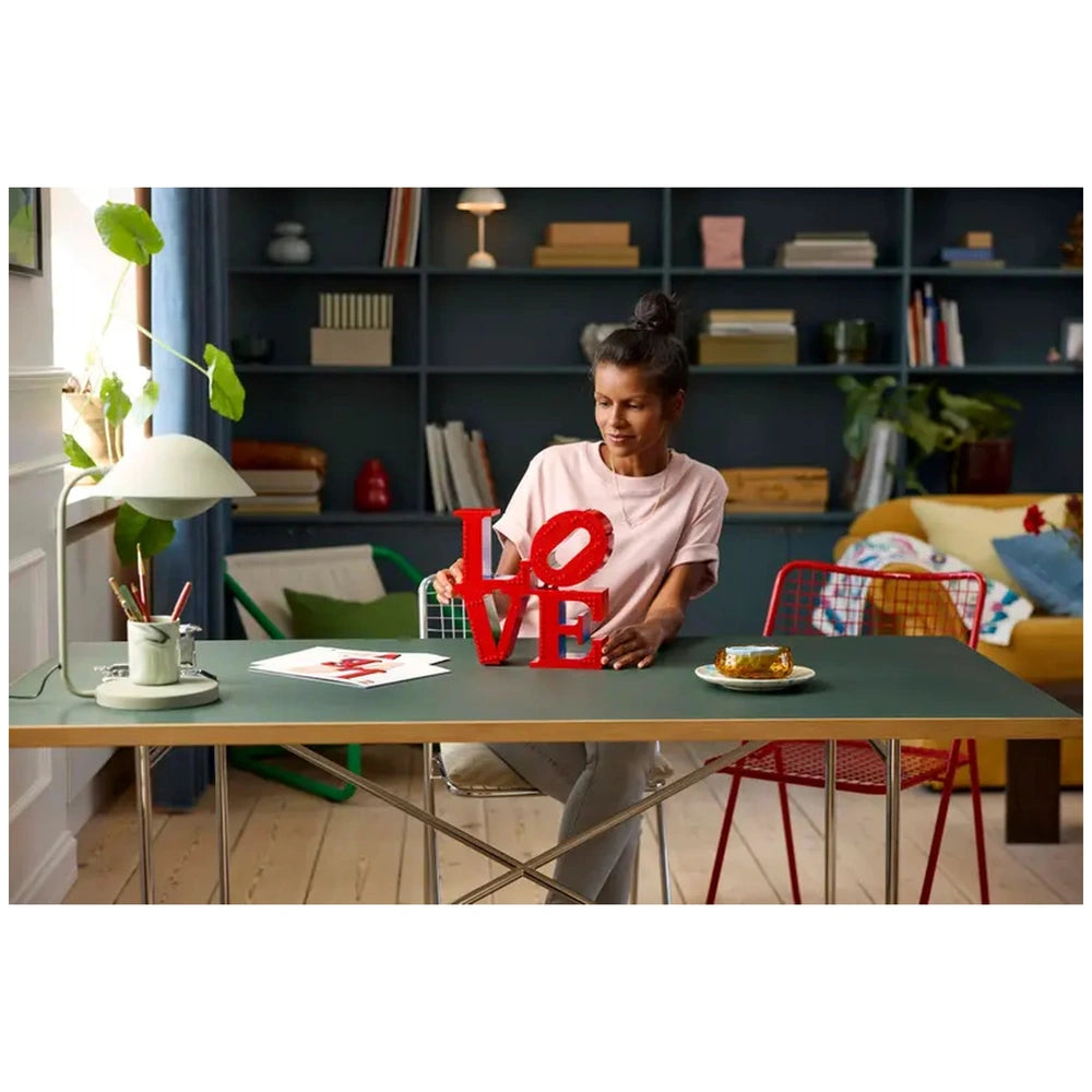 Lego Art LOVE construction set displayed on a green table with a woman holding a large red letter "L" and smiling.
