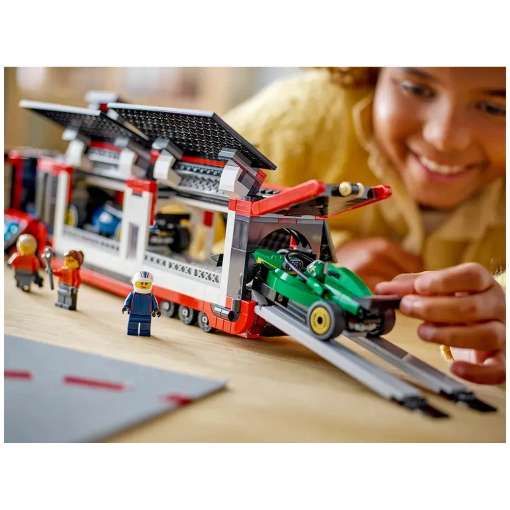 A child smiles while loading a green LEGO® F1® car onto a red and white transport truck, with miniature figures and cars nearby.