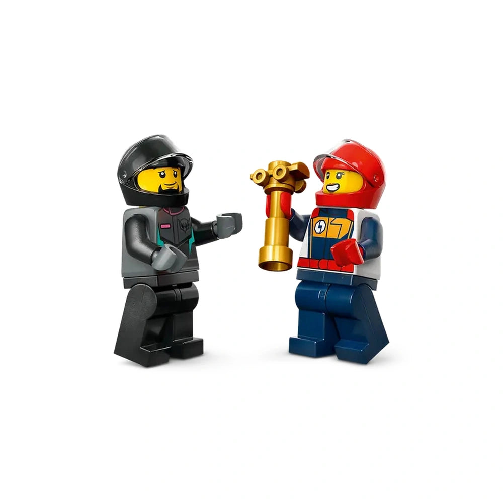 Two LEGO race driver minifigures celebrate victory, one holding a gold trophy. The first figure wears a black helmet and gray outfit, while the second dons a red helmet and colorful racing gear.