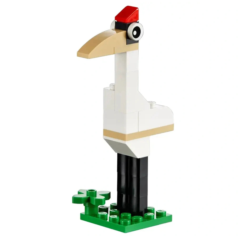 A whimsical LEGO creation of a stork standing on green baseplates, featuring a white body, beige accents, a long beak, and a red hat.