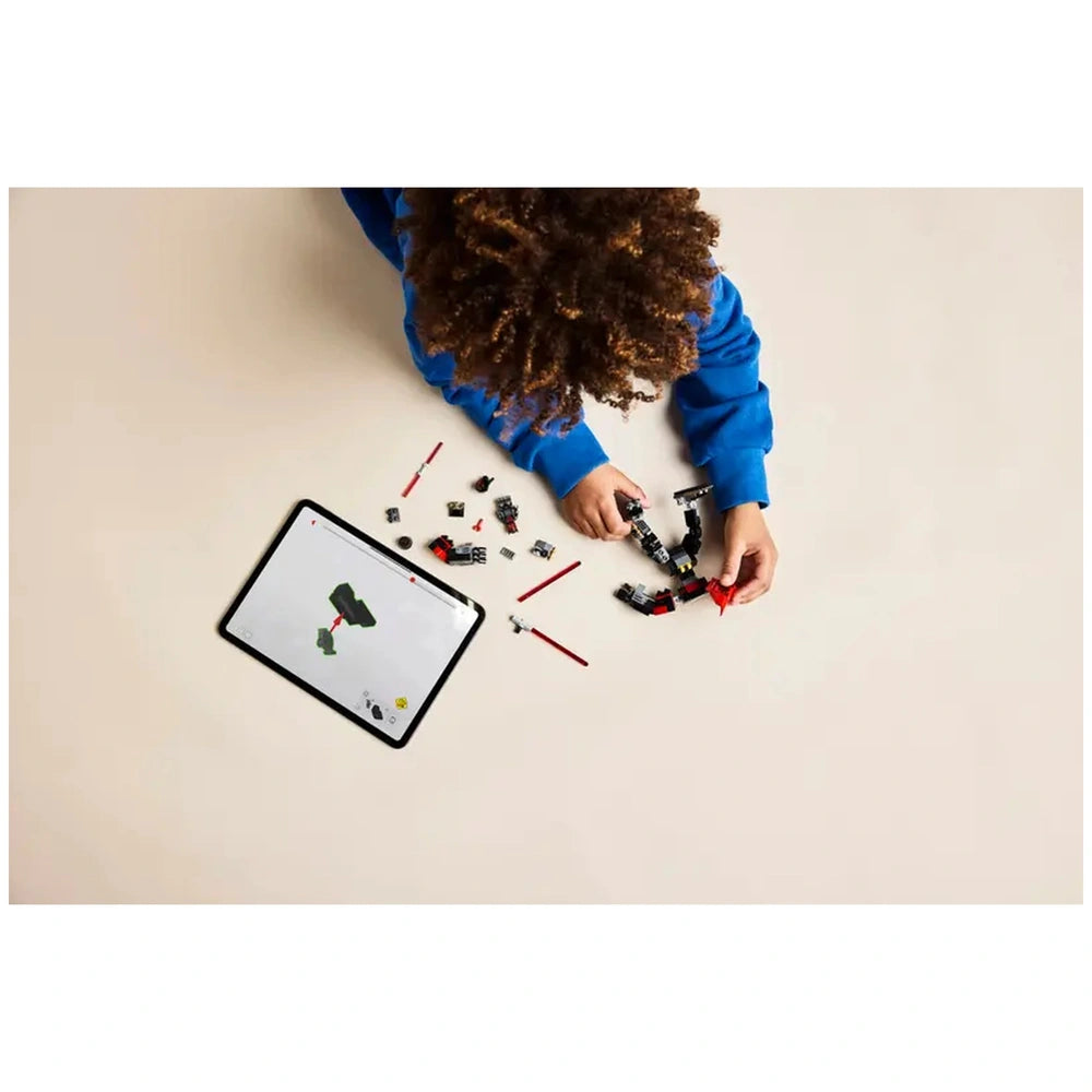 A child with curly hair in a blue sweater assembles the LEGO Darth Maul Mech, surrounded by various colorful bricks and a tablet showing building instructions.