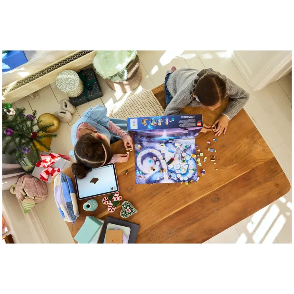 Two children creating with the LEGO Disney Frozen Advent Calendar 2025 on a wooden table, surrounded by colorful decorations and a small Christmas tree.