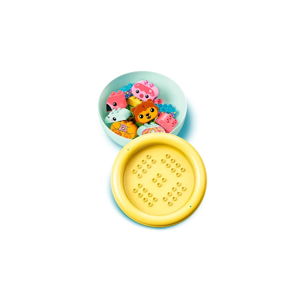 Colorful LEGO DUPLO floating animal figures, including a lion and flamingo, nestled in a light blue bowl beside a yellow strainer.