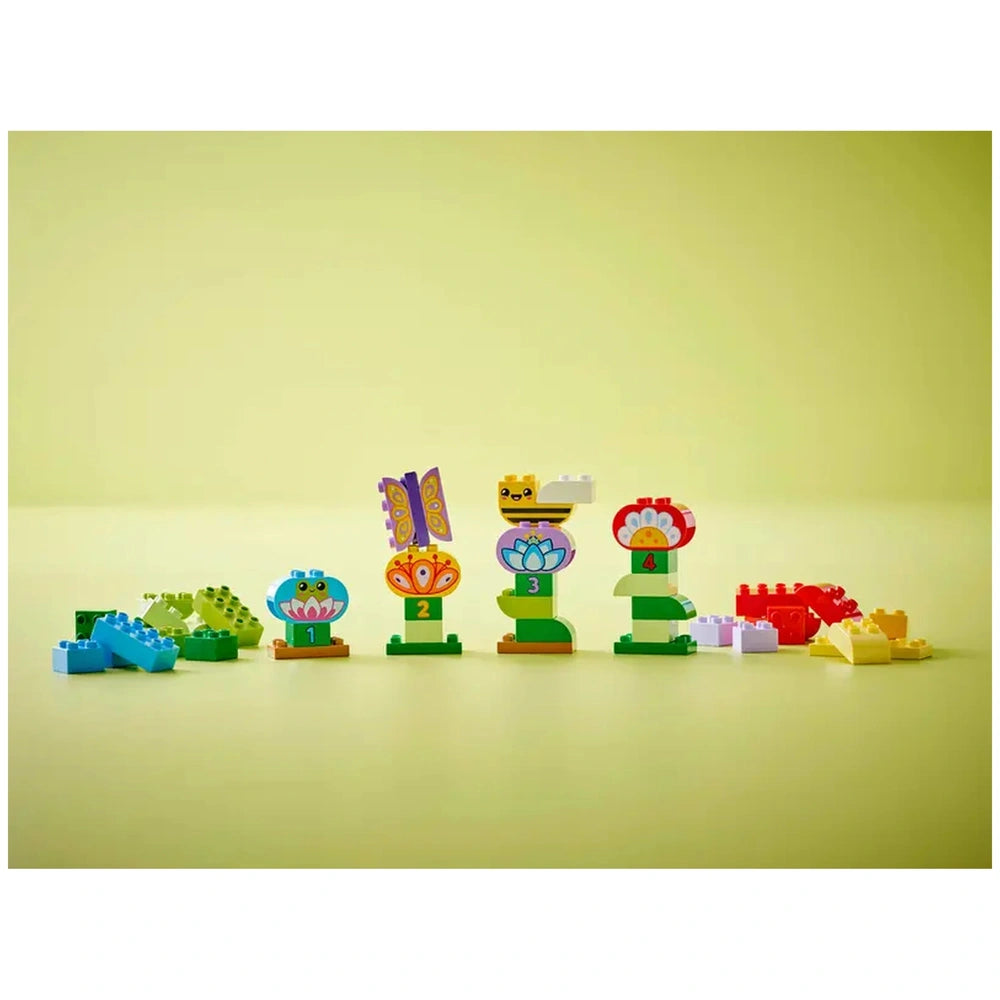 Colorful LEGO DUPLO flower and animal building set featuring a frog, butterfly, and bee, arranged against a soft green background.