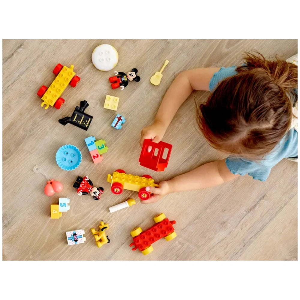 Child playing on a wooden floor with colorful LEGO DUPLO pieces, including Mickey and Minnie figures, a train, and number blocks.