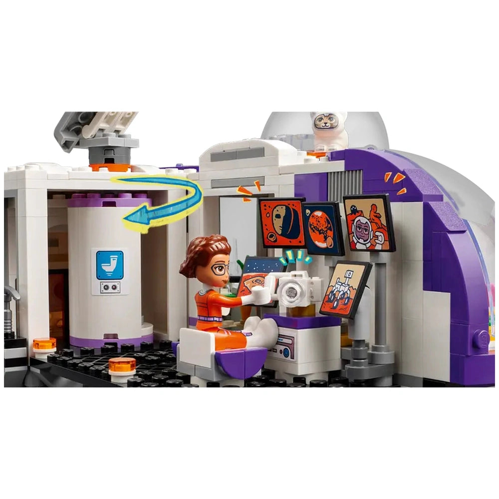 A mini-doll in an orange space suit sits at a monitor in a colorful Mars research base, surrounded by images of planets and astronauts.