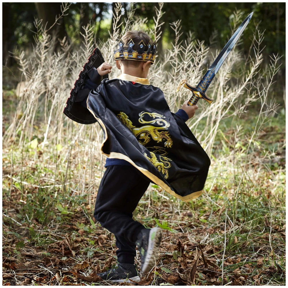 Young child in a shiny black cape with a yellow emblem and blue crown, holding a silver sword with a blue and gold handle.