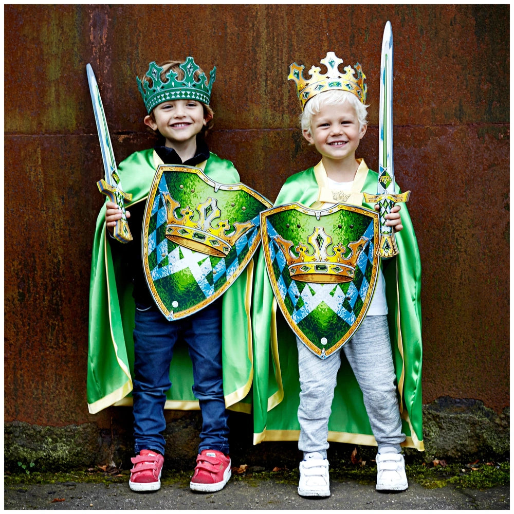 Liontouch Kingmaker crown worn by two children in green capes, holding green and gold swords against a rusted metal wall.
