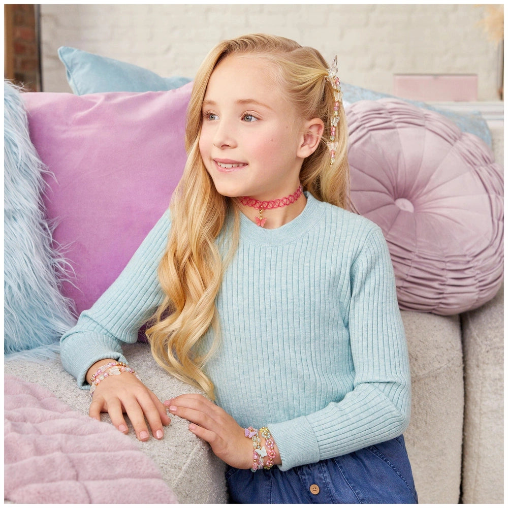 Butterfly jewelry set displayed on a girl wearing a light blue shirt and multicolored bracelets, with purple and pink pillows