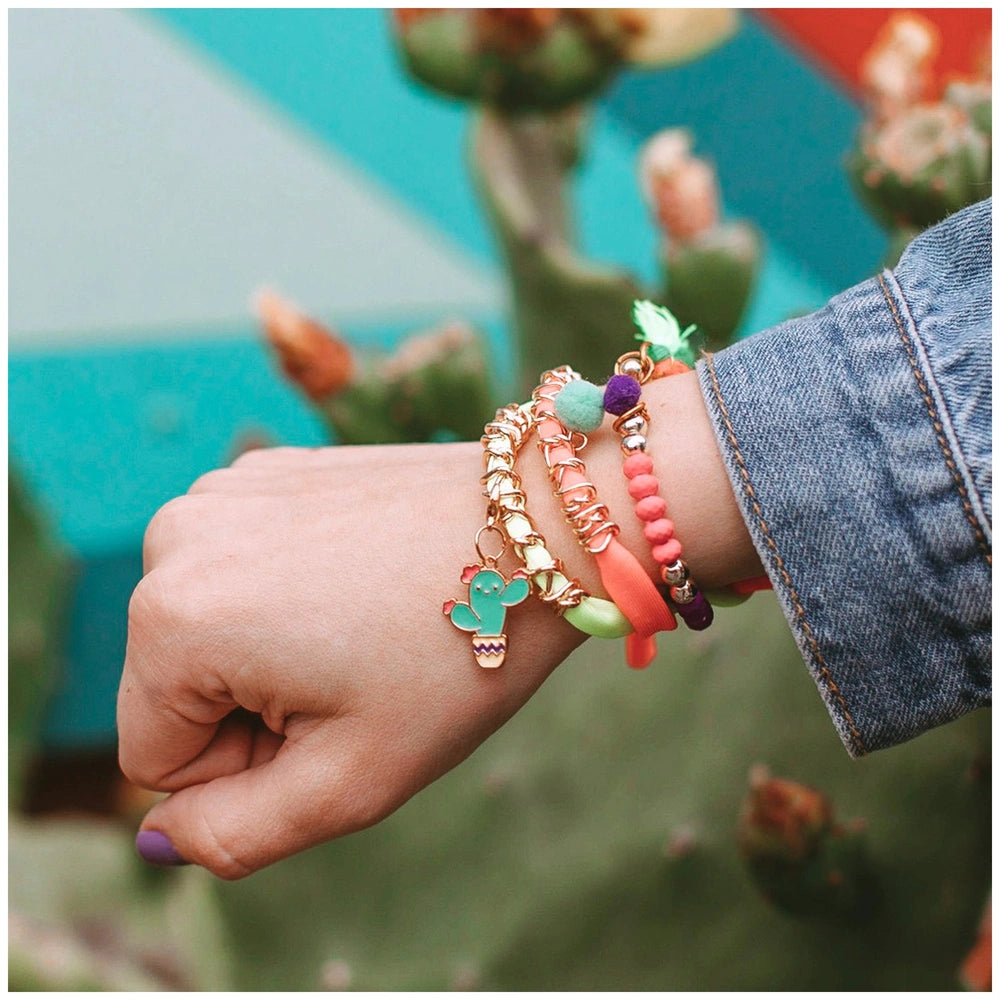 Neo-Brite bracelet with colorful strands and charms, including a dinosaur and cactus, worn by a hand in a denim jacket.