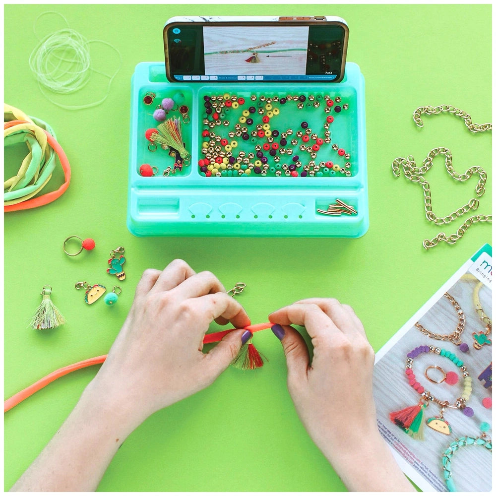 Neo-Brite Chains and Charms displayed on a bright green tabletop with colorful beads and jewelry components in various materi
